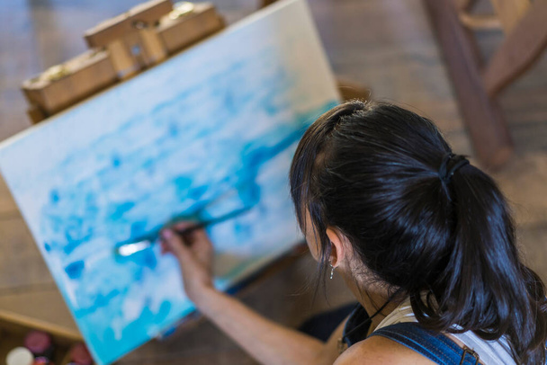 Donna artista pittura su una tela un dipinto astratto blu. Donna creativa che lavora sul pavimento nel suo studio d'arte. - Foto, immagini