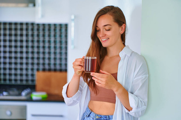Happy beautiful joyful carefree satisfied attractive woman drinking hot black tea at home kitchen - Foto, immagini