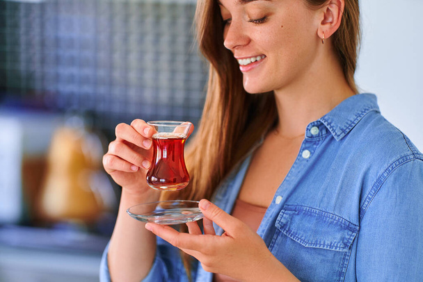 Beautiful satisfied smiling joyful happy female drinking traditional turkish tea at home kitchen  - Photo, image