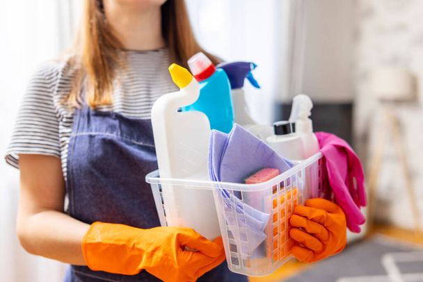 Woman in rubber gloves with basket of cleaning supplies ready to clean up her apartment. Housewife has many household chores, domestic work and professional cleaning service. Low depth of field - Fotó, kép