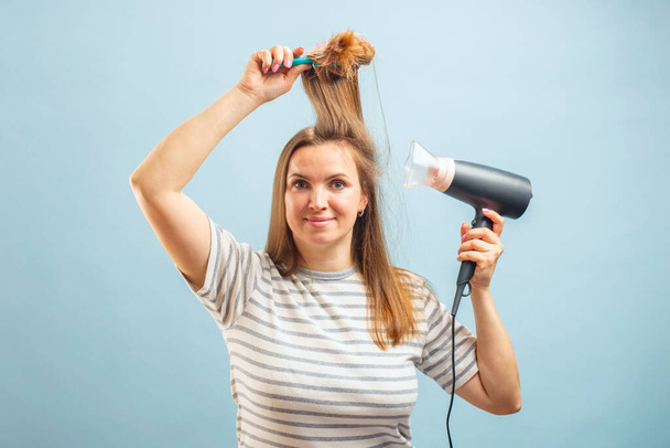 Young smiling woman using hair dryer on blue background. Hair style, hair care concept - Photo, Image
