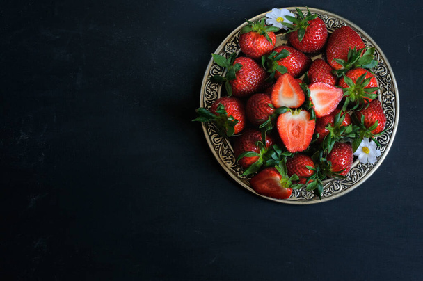 Reife Erdbeeren in einem schönen Teller auf schwarzem Hintergrund. Tageslicht, selektiver Fokus mit Kopierraum - Foto, Bild