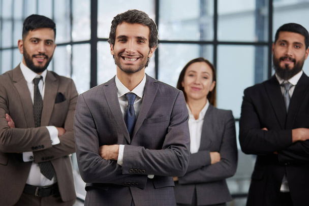 portrait shot of smiling business team of four standing and smiling at camera against a modern office background - Fotó, kép