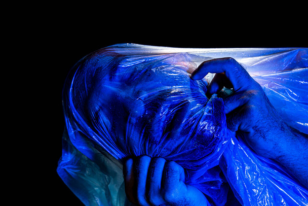 Homme avec un sac en plastique au-dessus de la tête, étouffé. Studio filmé avec filtre bleu. Isolé sur fond noir. - Photo, image