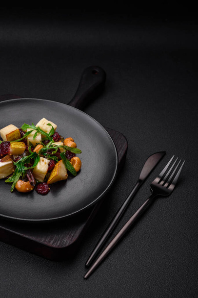 Ensalada vegana fresca deliciosa con pera, queso brie, nueces y granos, y rúcula en un plato de cerámica sobre un fondo oscuro - Foto, imagen