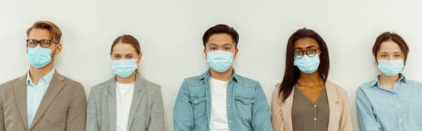 Personnes de race mixte portant un masque de protection faciale et posant contre un mur blanc - Photo, image