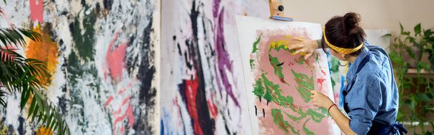 Visszapillantás tehetséges női művész dolgozik egy modern elvont olajfestmény. Ujjakkal festi a vásznat, és a műhelyben áll. Művészet, hobbi, szabadidős koncepció - Fotó, kép