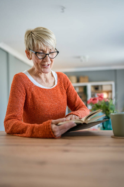Одна женщина взрослая старшая белая пенсионерка современная бабушка с короткими волосами читает книги на дому носить очки реального человека копировать пространство - Фото, изображение