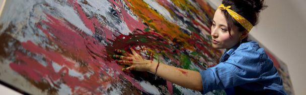Focused young woman, female painter creating a large modern abstract oil painting, applying paint on canvas with fingers. Art, hobby, leisure concept - Foto, Bild