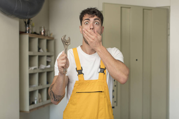 young handsome man covering mouth with a hand and shocked or surprised expression. handyman concept - Фото, зображення