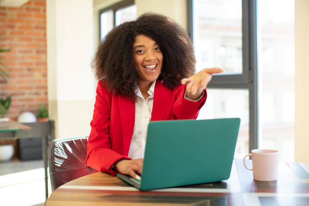 mujer negra bastante afro sonriendo felizmente y ofreciendo o mostrando un concepto. concepto de mujer de negocios y portátil - Foto, Imagen