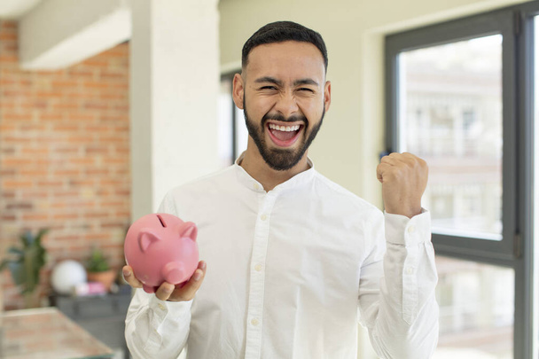 young  adult man feeling shocked,laughing and celebrating success. piggybank concept - Фото, зображення