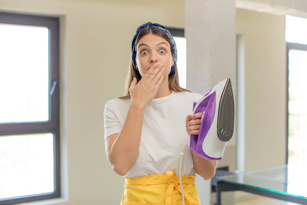 young pretty woman covering mouth with a hand and shocked or surprised expression. housekeeper and laundry concept - Photo, Image