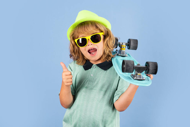 Excited child with thumb up. Funny happy kid in casual wear holding longboard looking happy and excited. Studio isolated portrait of kid with skateboard - Photo, Image