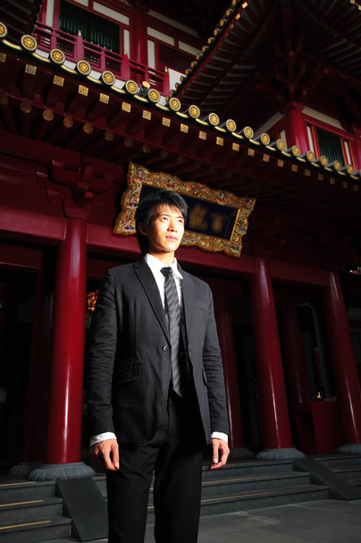 Aasialainen nuori mies seisoo temppelin edessä
 - Valokuva, kuva