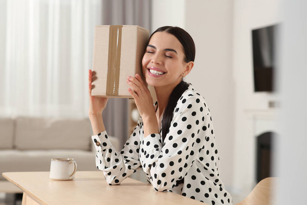 Happy young woman with parcel at table indoors. Internet shopping - Foto, Bild