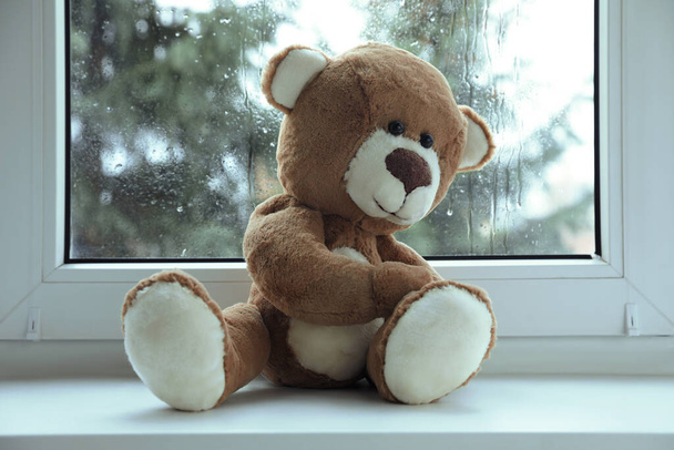 Cute lonely teddy bear on windowsill indoors - Zdjęcie, obraz