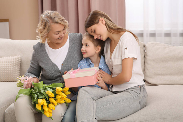 Little girl congratulating her mom and granny with flowers and gift at home. Happy Mother's Day - Фото, зображення