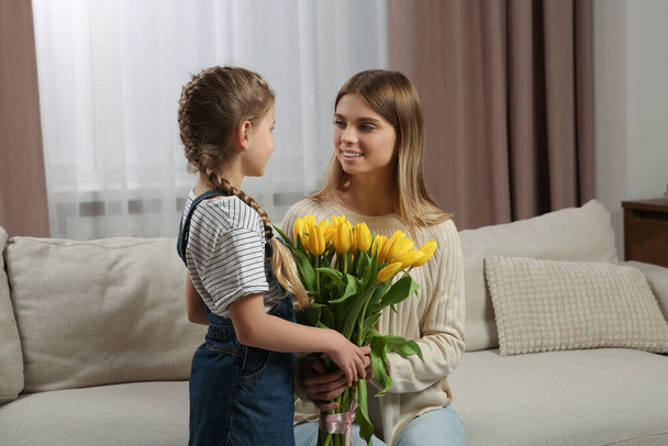 Little daughter congratulating mom with bouquet of yellow tulips at home. Happy Mother's Day - Фото, зображення