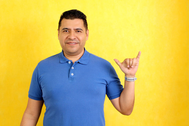 Hombre adulto latino moreno utiliza lenguaje de señas típico de las personas sordas para establecer un canal de comunicación con su entorno social - Foto, imagen