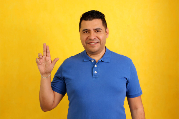 Ciemnowłosy Latynos dorosły mężczyzna używa języka migowego typowego dla osób głuchych, aby stworzyć kanał komunikacji ze swoim otoczeniem społecznym. - Zdjęcie, obraz