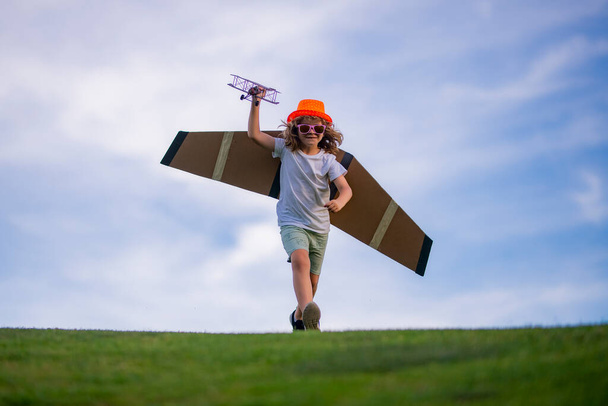 Bambino bambino bambino giocare con le ali di aeroplano giocattolo e sognare il futuro. Il concetto di gentilezza del bambino e dell'infanzia. I bambini corrono con l'aereo sul campo - Foto, immagini