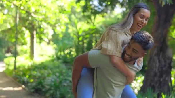 Love, nature and piggy back for happy couple walking in garden and bonding on summer weekend together. Interracial happiness, woman jumping on man with smile and laugh on fun or romantic date in park. - Footage, Video