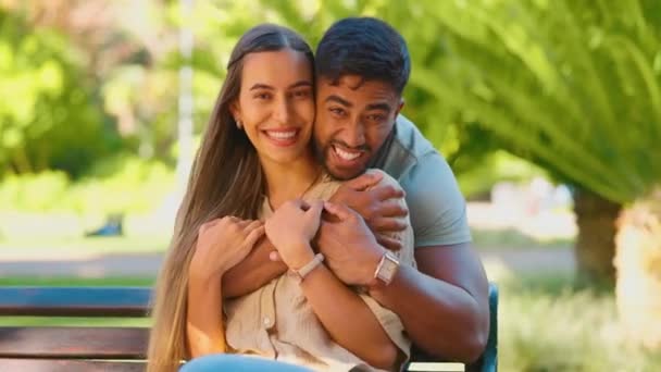 Park, love and face of interracial couple hug for bonding, quality time and relax on bench for weekend date. Nature, dating and portrait of happy man and woman for embrace, commitment and romance. - Footage, Video