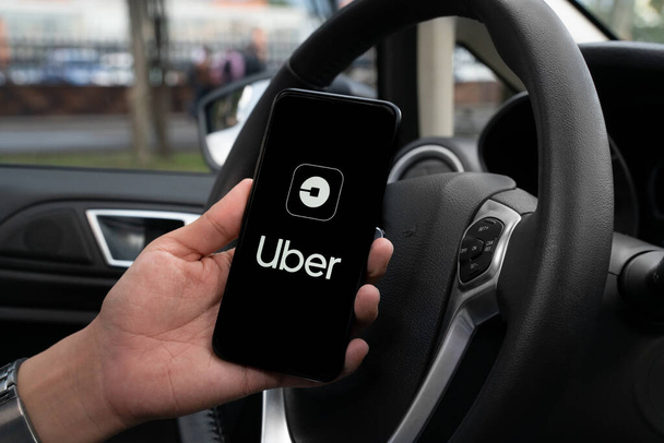 Uber driver holding smartphone in car. Uber is an American company offering transportation services online. Uber APP - Fotografie, Obrázek