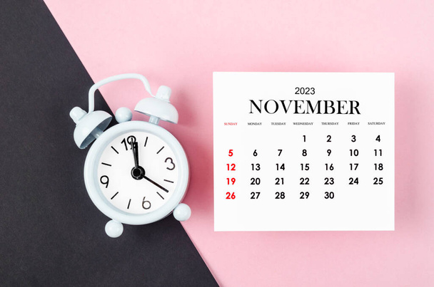 November 2023 Monthly calendar year with alarm clock on pink and black background. - Foto, imagen