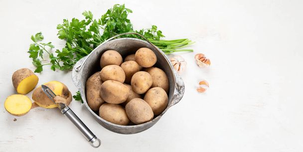 Raw potato food. Fresh potatoes in an old cooking pot on a white background. Top view. Panorama with copy space. - Foto, afbeelding