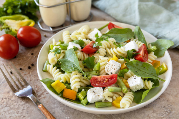 Salad with gluten free pasta, spinach, tomatoes, beans and feta cheese on a stone table. Italian food. Healthy food, vegetarian appetizer. - Photo, image