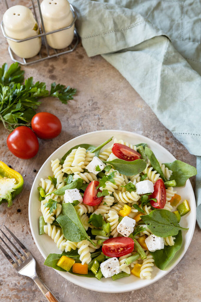 Italian food - Salad with gluten free pasta, spinach, tomatoes, beans and feta cheese on a stone table. Healthy food, vegetarian appetizer.  - Fotoğraf, Görsel