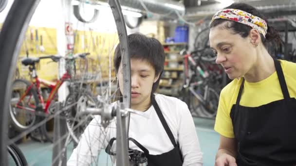 twee vrouwen in multiraciale gemeenschap fiets workshop, een leren de andere hoe het fietswiel uit te lijnen, concentreren op het controleren van de fiets. - Video