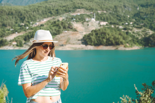 Nainen tekstailee verkossa matkapuhelimella vuorten järven tausta. Matkailija nainen chat viestejä matkapuhelimeen sinisellä järvellä ulkona matkustaa seikkailu loma. Älypuhelimen käyttö - Valokuva, kuva