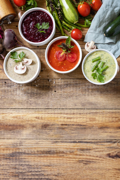 Healthy food. Autumn set of different vegetable soups. Vegan hot cream soups (tomatoes, mushrooms, beets, green beans) on rustic wooden table. View from above. Copy space. - Photo, Image