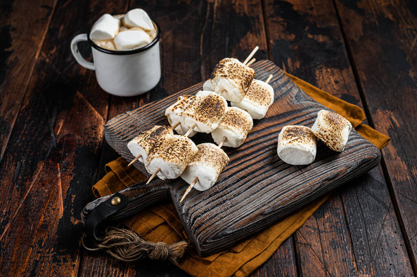 Roasted Marshmallow on the sticks with Cup of coffee on wooden board. Wooden background. Top view. - Photo, image