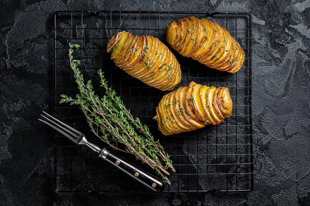 American traditional Homemade Hasselback Potato with Fresh Herbs. Black background. Top view. - Foto, Bild