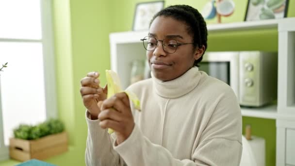 Afričanky americká žena usměvavá sebevědomě jíst banán v jídelně - Záběry, video