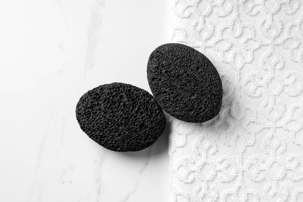 Black volcanic pumice stone lies on the table next to a white towel. - Foto, Bild
