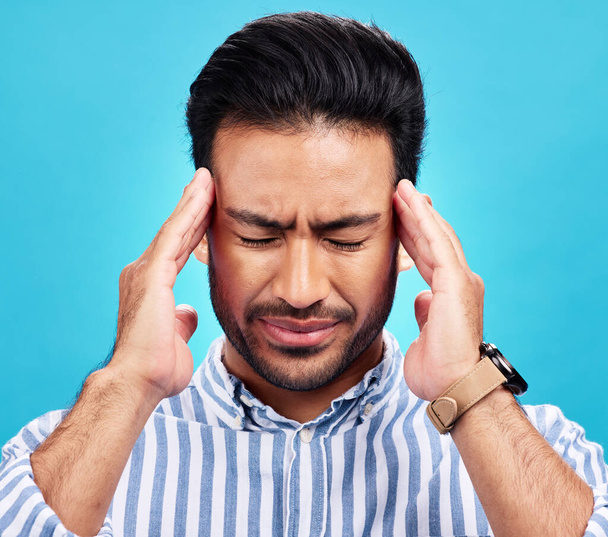 Man with headache, pain and stress with anxiety and mental health problem or crisis isolated on blue background. Male person hands holding head, massage temple with depression and migraine in studio. - Photo, Image