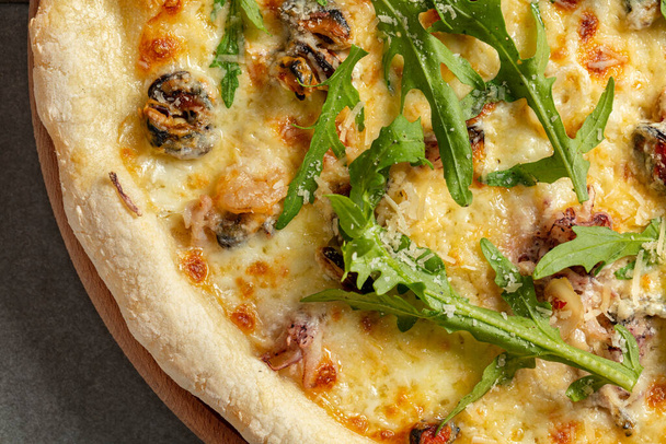 Sourdough pizza with mussels, shrimps, cream cheese sauce, arugula leaves and parmesan cheese. Pizza lies on a gray stone background. - Foto, Bild