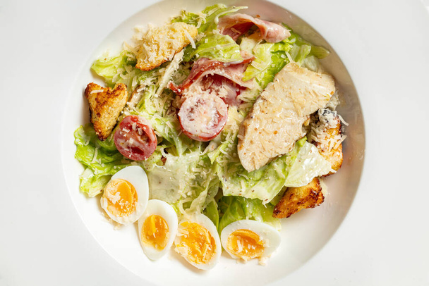 Caesar salade met kip, kerstomaten, croutons, kwarteleitjes, sla en knoflooksaus in een lichte keramische plaat. De plaat staat op een grijze stenen achtergrond. - Foto, afbeelding