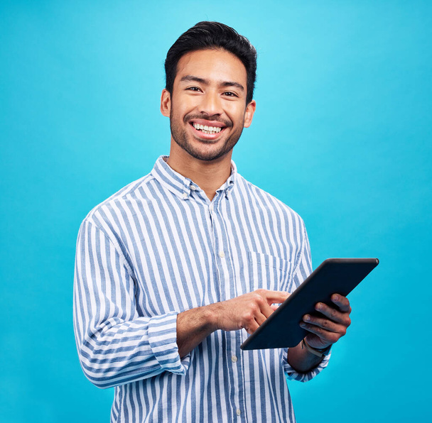 Tablet, Asian man and smile portrait in a studio on social media, internet and website app scroll. Happiness, isolated and blue background with a male model reading technology for digital networking. - Fotografie, Obrázek