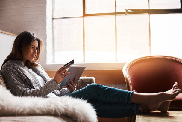 Залишайтеся і насолоджуйтеся перевагами онлайн-покупки. приваблива молода жінка використовує цифровий планшет і кредитну картку на дивані вдома
 - Фото, зображення