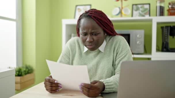 Африканская женщина с плетеными волосами читает документ, страдающий от головной боли в столовой - Кадры, видео