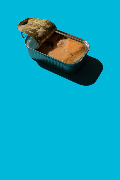 Open tin can with salmon on a blue background with hard shadows, the concept of red canned fish on the sea or in the ocean - Fotó, kép