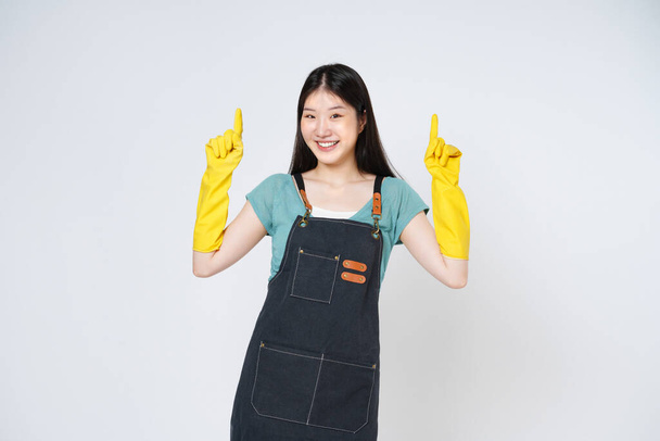 Portrait of young woman wearing yellow rubber gloves for hands protection and pointing to empty copy space isolated on white background. - Fotografie, Obrázek