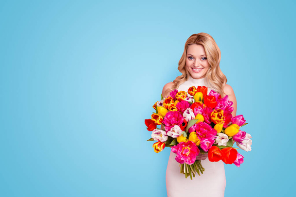 Portrait with copyspace, empty, place of gorgeous positive woman in white dress having big bouquet of tulips in hands looking at camera isolated on pink background. - Foto, Bild