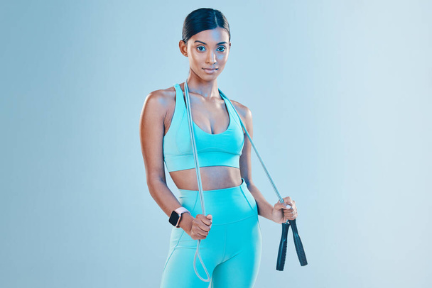 Fitness, skipping rope and mockup with a sports woman in studio on a blue background for health or wellness. Exercise, mindset and space with a young female athlete training for cardio or endurance. - Photo, Image
